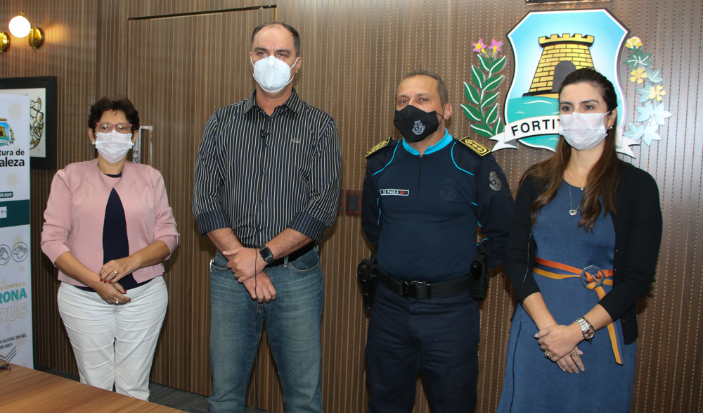 Dolores Fernandes, Coronel Holanda, Coronel De Paula e Laura Jucá em pé lado a lado, de máscara, posando para a foto com brasão da Prefeitura ao fundo